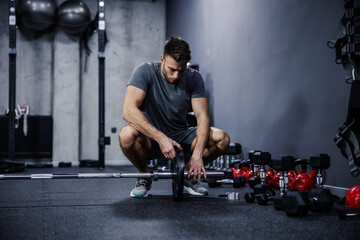 Dark atmosphere gym with sports equipment. A portrait of a handsome and fit man squatting in the...