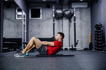 The importance of breathing during training. A handsome young male person performs abdominal exercises and sighs properly and exhales. Healthy fitness habits and sports routines. Modern indoor gym