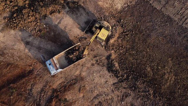 Aerial view of a wheel loader excavator with a backhoe loading sand onto a heavy earthmover at a construction site.