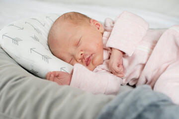 A Caucasian newborn baby girl is sleeping peacefully in her baby lounger in a pink outfit. Sleeping...