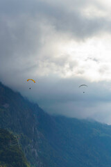 A pair of paragliders float through a cloudscape in Interlaken