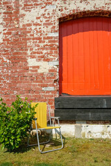 Fototapeta na wymiar Red factory door in brick wall with yellow folding chair
