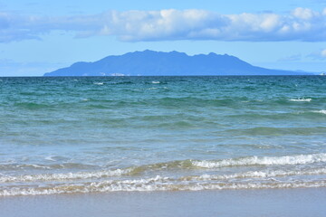 Little Barrier Island behind oceanic sandy beach with mild surf. Location: Tawharanui Peninsula New Zealand