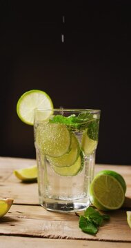 Vertical video of close up of drink with limes on black background, with copy space
