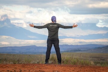 Young male hiker with open arms on the ground observing the Gran Sabana tepuis in the background, Venezuela.
