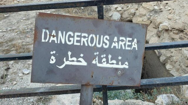 A warning sign with dangerous area in English and Arabic near a steep drop off in desert location of Jordan in Middle East
