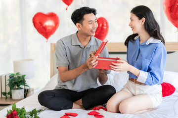 Asian couple Showing love surprise giving flowers or gifts to each other on important occasions such as Valentine's Day birthdays or wedding anniversaries with love and warmth in bedroom of their home