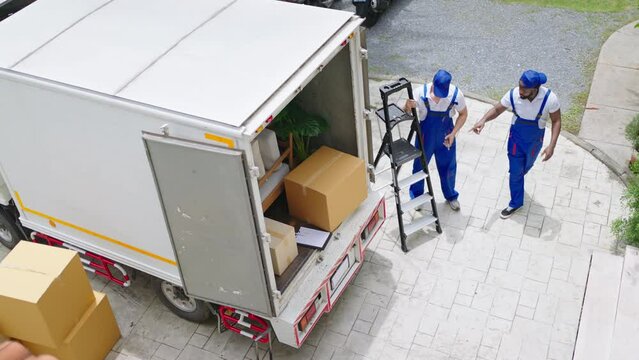 top view of Workers unloading boxes from van outdoors.House move, mover service and Moving service concept.Two young handsome worker wearing uniforms are unloading the van full of boxes.4k UHD video