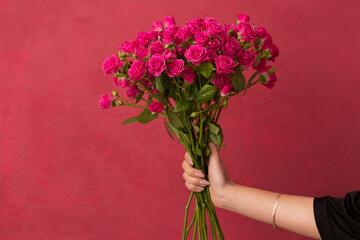 bouquet of pink roses in female hands on a pink background