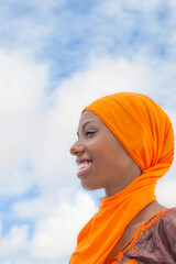 
Beautiful teenage girl smiling and wearing an embroidered dress and and orange headscarf, 18 years old, blue sky, white clouds, photo