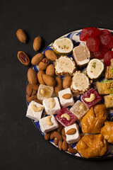 A large plate of oriental sweets and nuts on a dark background