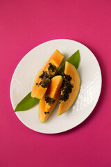 juicy papaya cut into pieces in a plate on a pink Viva Magenta color background