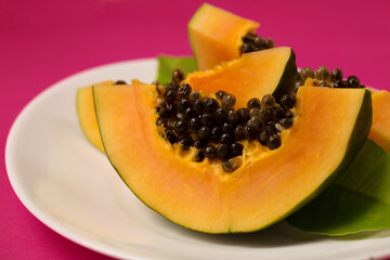 Fresh juicy papaya in a plate on a pink Viva Magenta color background