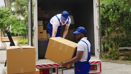 Workers unloading boxes from van outdoors.House move, mover service and Moving service concept.Two young handsome smiling workers wearing uniforms are unloading the van full of boxes.