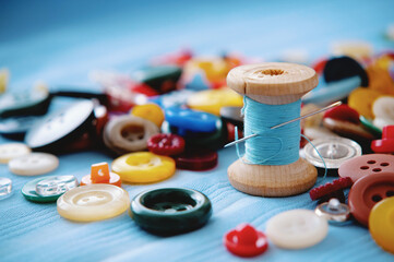 A bunch of colored buttons and a spool of thread and a needle. Tailor