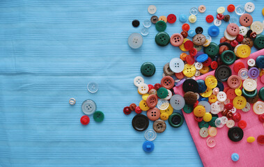 A lot of colored buttons for clothes on a blue fabric. Tailoring