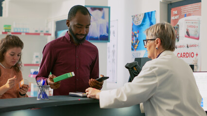 Diverse people buying pharmaceutical products at cash register, paying with smartwatch, mobile phone with nfc and credit card. Customers having pills and medicaments at counter.