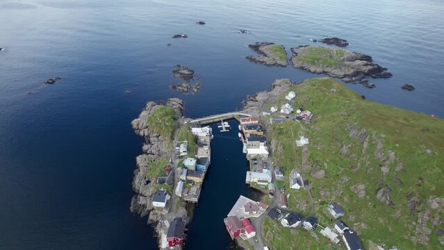 Aerial dolly forward view of a small fishing village around a small sheltered harbor on a rocky peninsula in Northern Norway, above the arctic circle