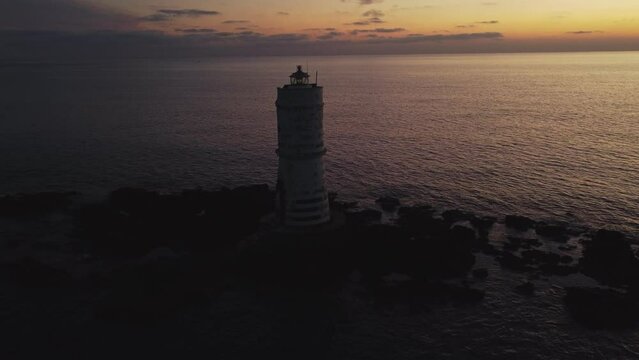 Aerial drone flying towards offshore Lighthouse on rocks in Calasetta, dusk