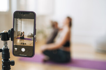 Young woman with little daughter fitness blogger doing exercises and recording video on mobile phone phone in studio