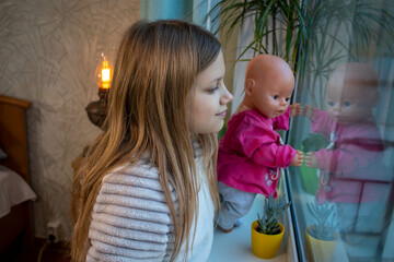 a little girl and her doll are looking out the window
