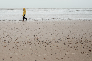 ein Mensch im gelben Regenmantel geht am Strand spazieren