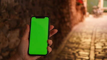 Female hands holding smartphone with green screen. Woman using mobile phone while walking in the street. Chroma key, close up female hand holding phone with vertical green screen