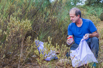 man crouching with garbage bags cleaning up the waste mountain
