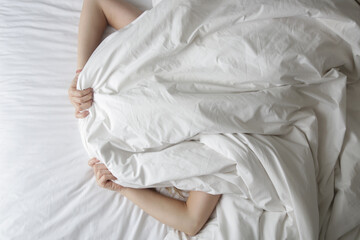 Fototapeta na wymiar Girl lying in bed covering her face with blanket
