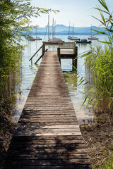Pier on the shore of the lake Chiemsee. View of moored ships and mountains. Beautiful nature in the middle of summer.