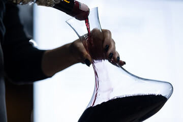 Close-up of the hands of a female bartender who pours wine from a bottle into a decanter on a light background