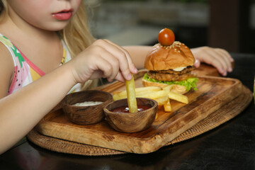 Little girl eating french fries with tomato sauce at the restaurant
