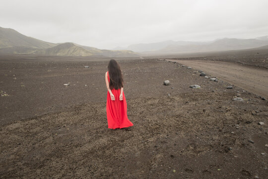 rear view of woman in red dress standing on cold and windy highland planes on lava in Iceland