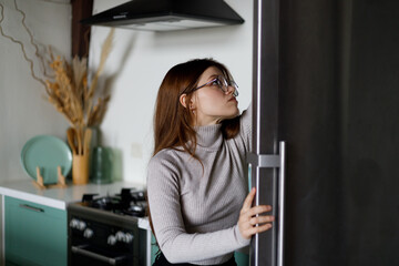 A woman after work chooses food in a black refrigerator in the kitchen, diet.