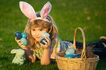 Easter kid in park. Child boy hunting easter eggs in spring lawn laying on grass. Child bunny boy with rabbit bunny ears.