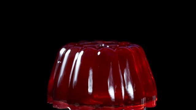 The red jelly rotates close-up on a black background, I hit it from above with a spoon so that droplets fly and it wobbles. Slow Motion
