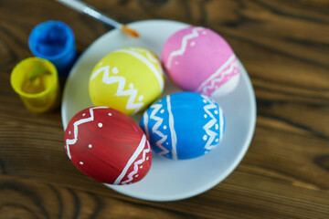 Fototapeta na wymiar Easter eggs on a white saucer with a brush and paint cans on a wooden background. Beautiful Easter background.