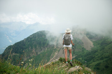 
Woman with backpack and trekking poles hiking in mountains, standing on cliff and enjoying the scenic view