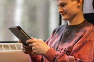 Smiling young man reading e-book when he traveling by train. Man sits at the train window and using digital tablet.