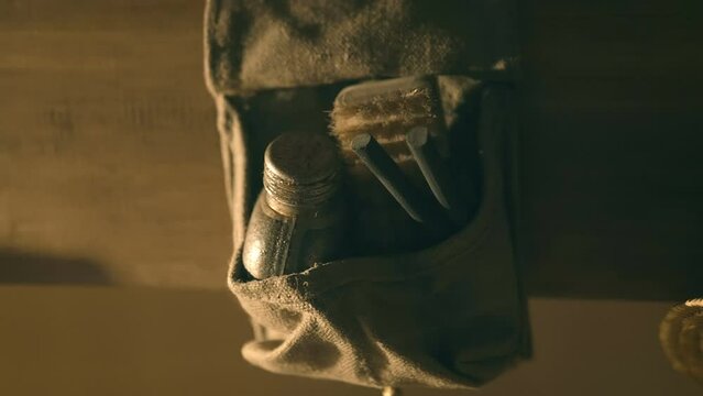 Hanging on a wooden beam on the wall is a small archaeologist's travel bag with a flask of water, an excavation brush, and a survival kit with flint rods to start a fire. Sepia tone. Shot in motion. C