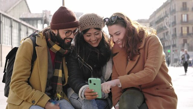 Group of friends sitting together using mobile phone to share content on social media in winter 