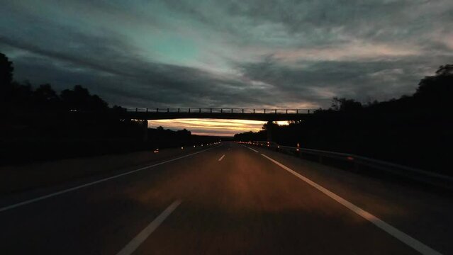 Driving on empty long asphalt road in the night with dusk sunset in background over a cloudy sky. Travel truck car expedition destination. Transport with vehicle on the road. Bridge on freeway