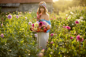 Portrait of a young stylish woman stands with a basket full of colorful freshly picked up dahlias...
