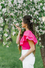 Happy to a young beautiful woman in a spring garden holding a branch of apple blossoms and sniffing flowers