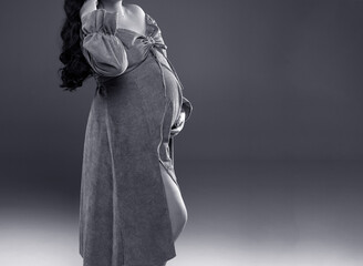 A pregnant girl in a dress holds her belly. A pregnant woman with long hair stands on a gray...