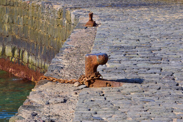 poller am hafen mit kette und rost auf einer steinmauer
