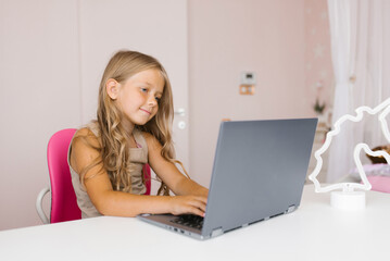 Cute little girl playing on a laptop at home. Home schooling and education, online learning, distance learning, homework, lifestyle concept of schoolgirls