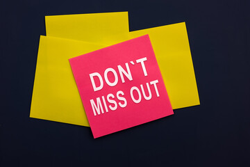 Don't miss out - inscription of a pink square sticky note paper on dark background. Top view. Life...