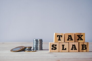 Tax slab written on wooden blocks with coins on desk. 