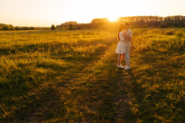 Wide shot of loving young couple in relationship hugging and kissing enjoying each other in wonderful sunlight of sunset on green meadow. Happy man and woman spending unforgettable moments together.